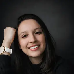 Natiele Soardi, sorrindo, apoiada na mão, em fundo escuro